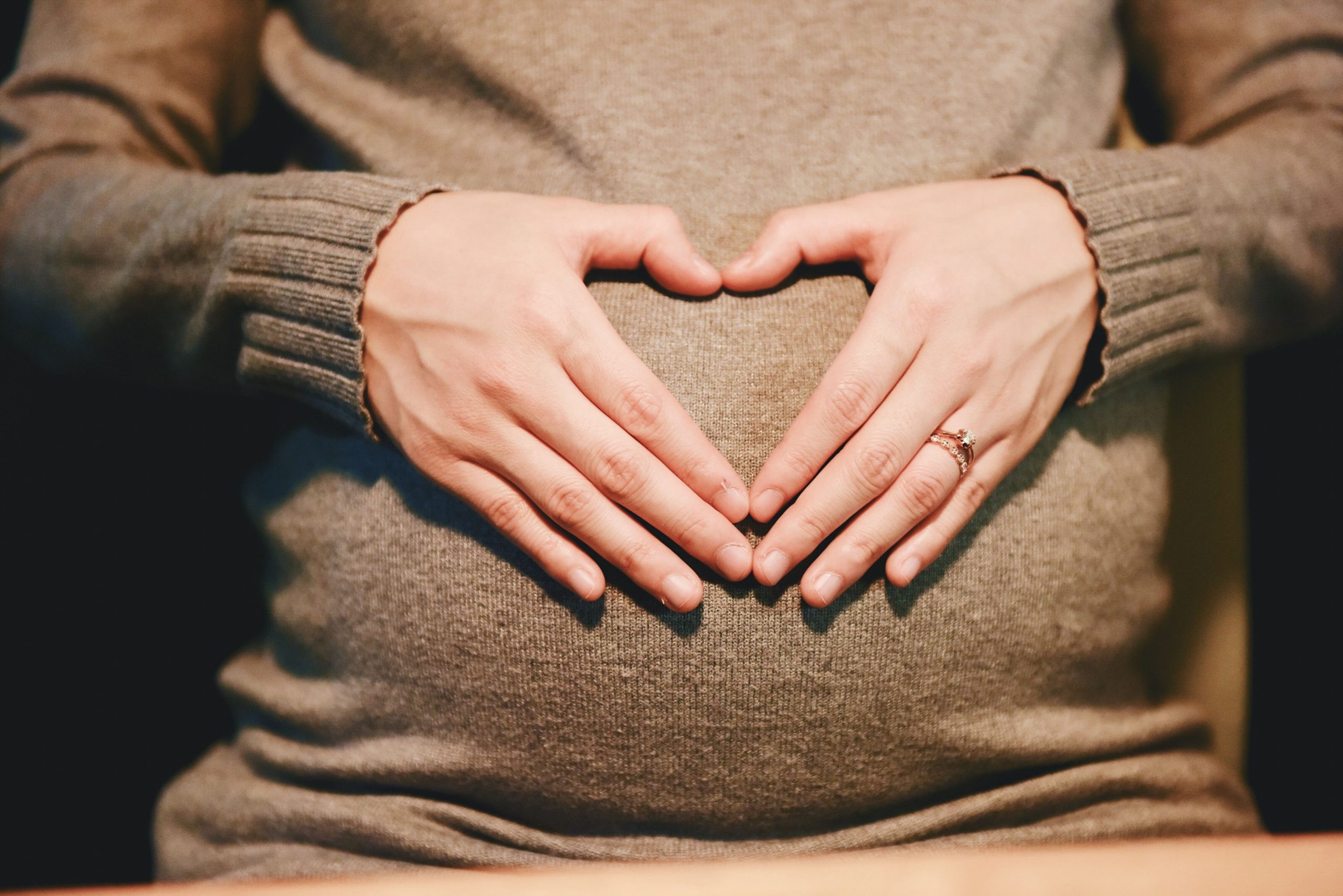 Foto einer Person die ihre Hände herzförmig auf ihren schwangeren Bauch gelegt hat.